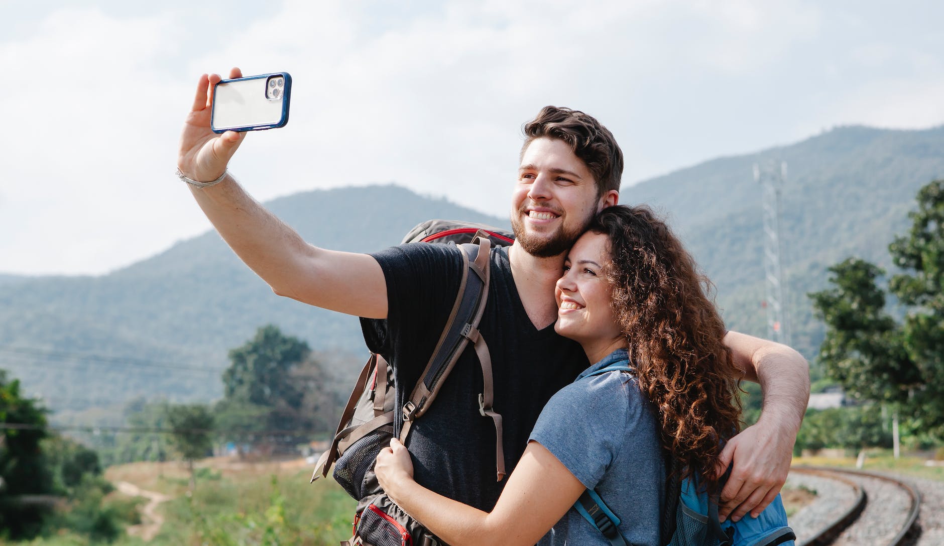 happy couple of travelers taking selfie on smartphone in nature in daytime