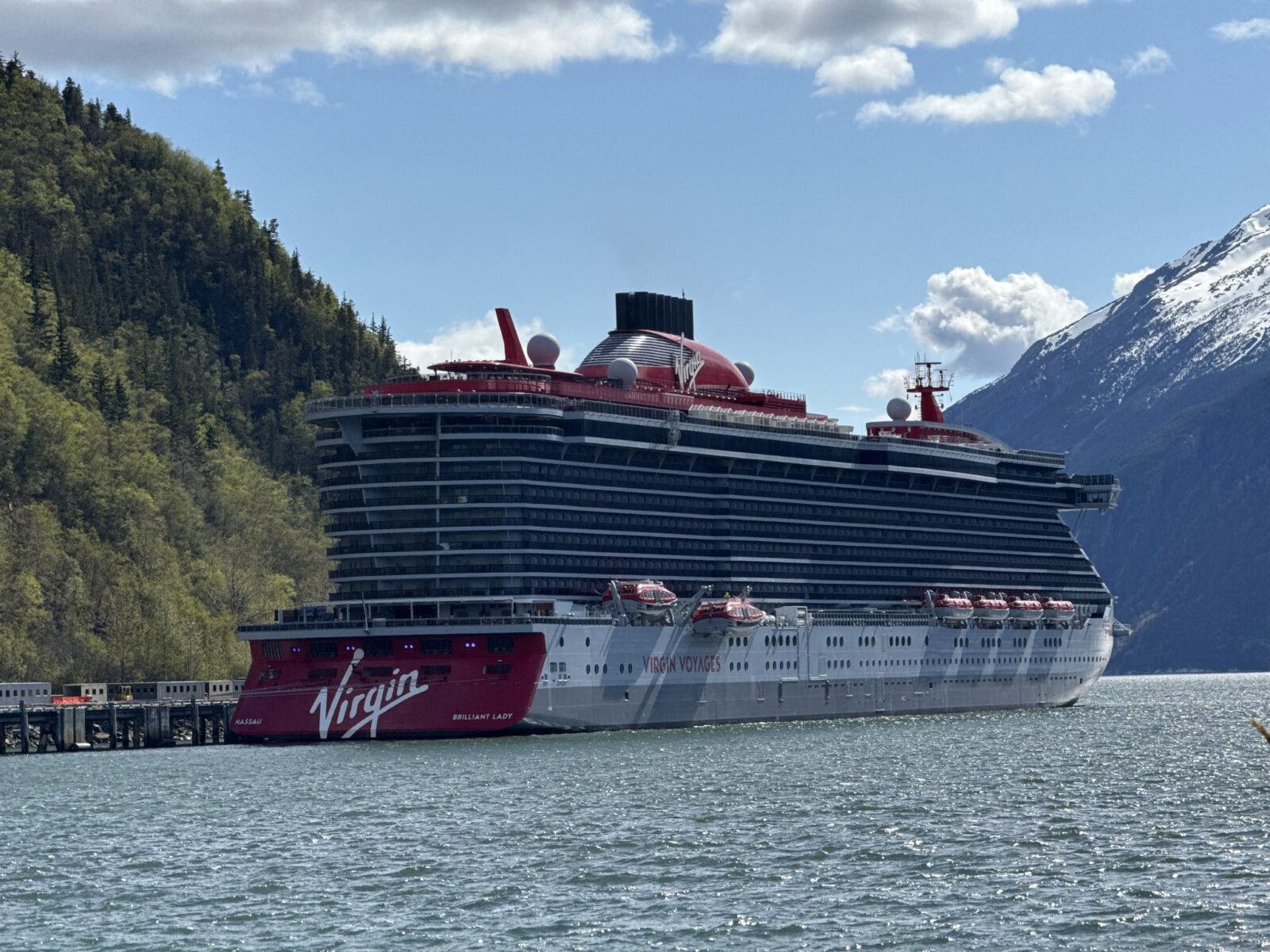Virgin Voyages Brilliant Lady docked in Alaska beneath snow-capped mountains