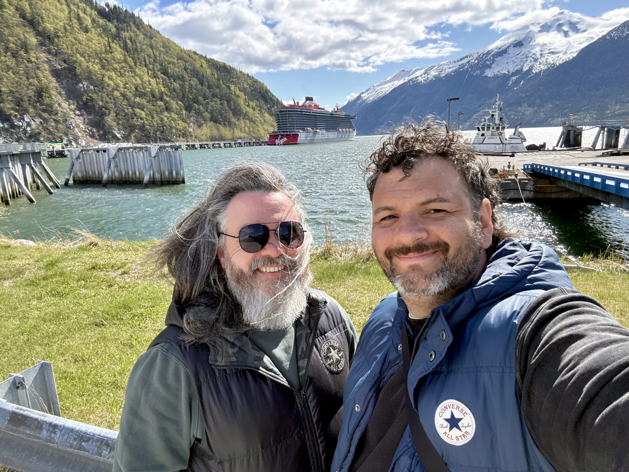 Kieran and Phil in port in Alaska with snow-capped mountains and the harbour behind them