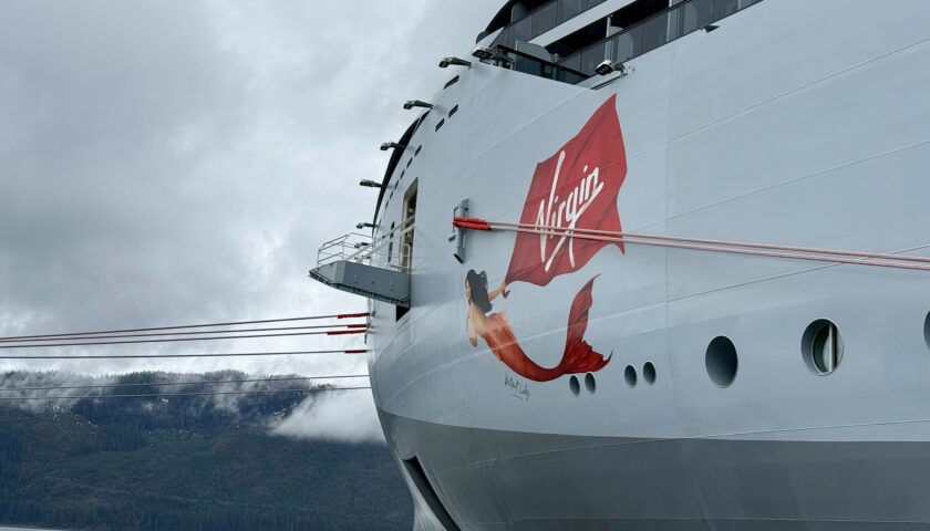 Virgin Voyages Brilliant Lady with its red logo docked at the Icy Strait Point pier