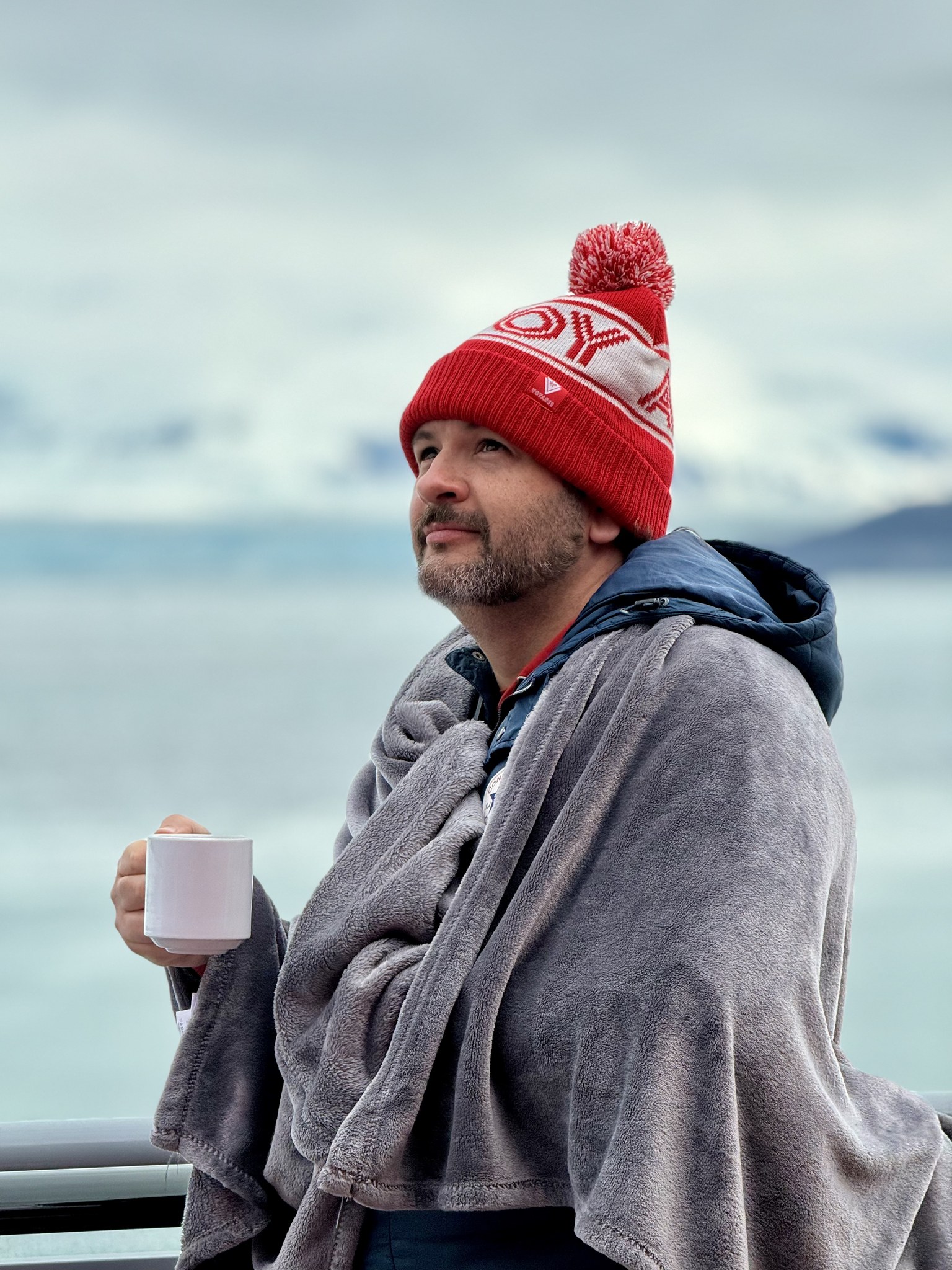 Wrapped up in a blanket and bobble hat with a hot drink on deck on glacier day