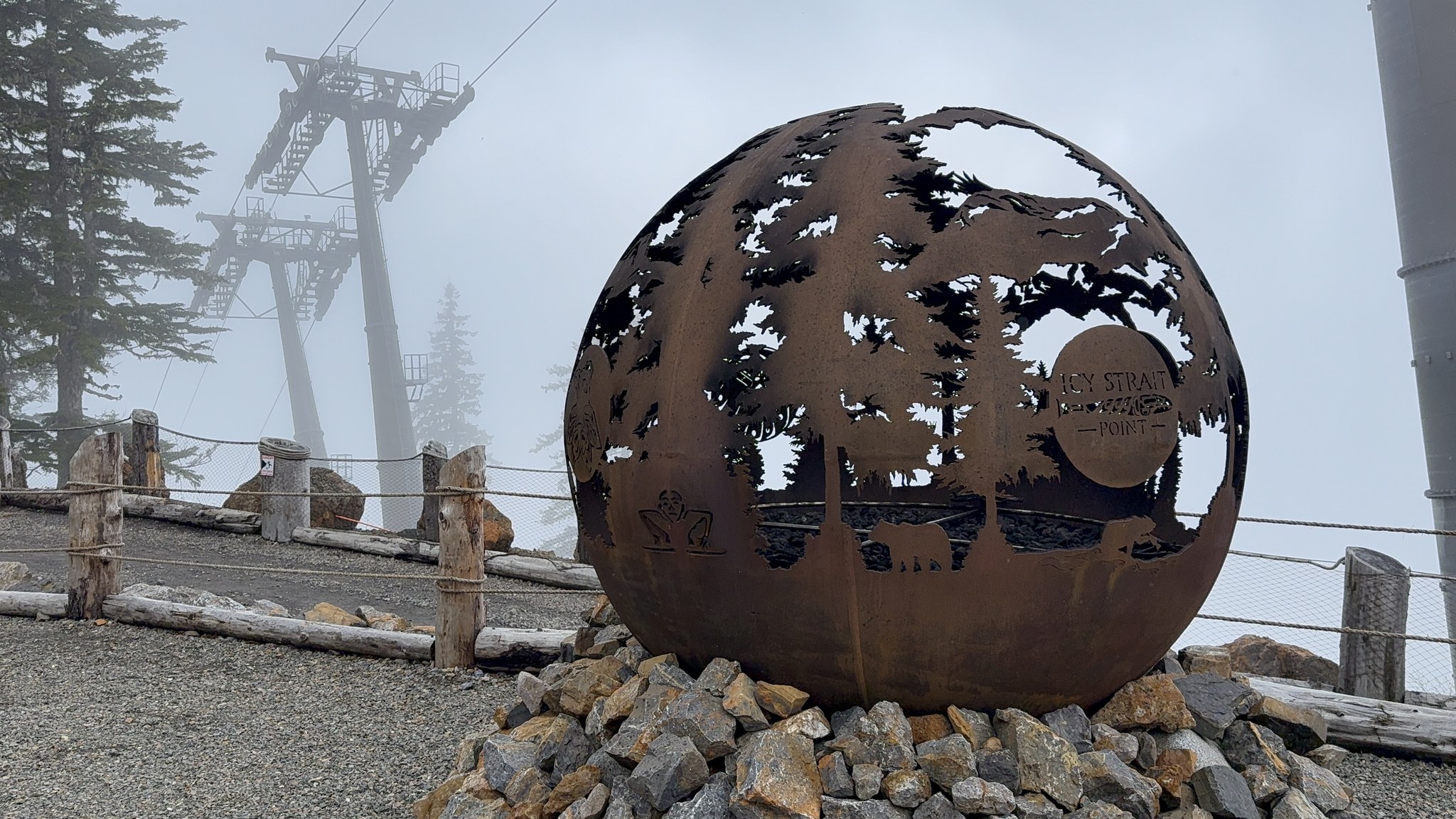 Metal globe sculpture with the gondola line behind, top of Hoonah Mountain