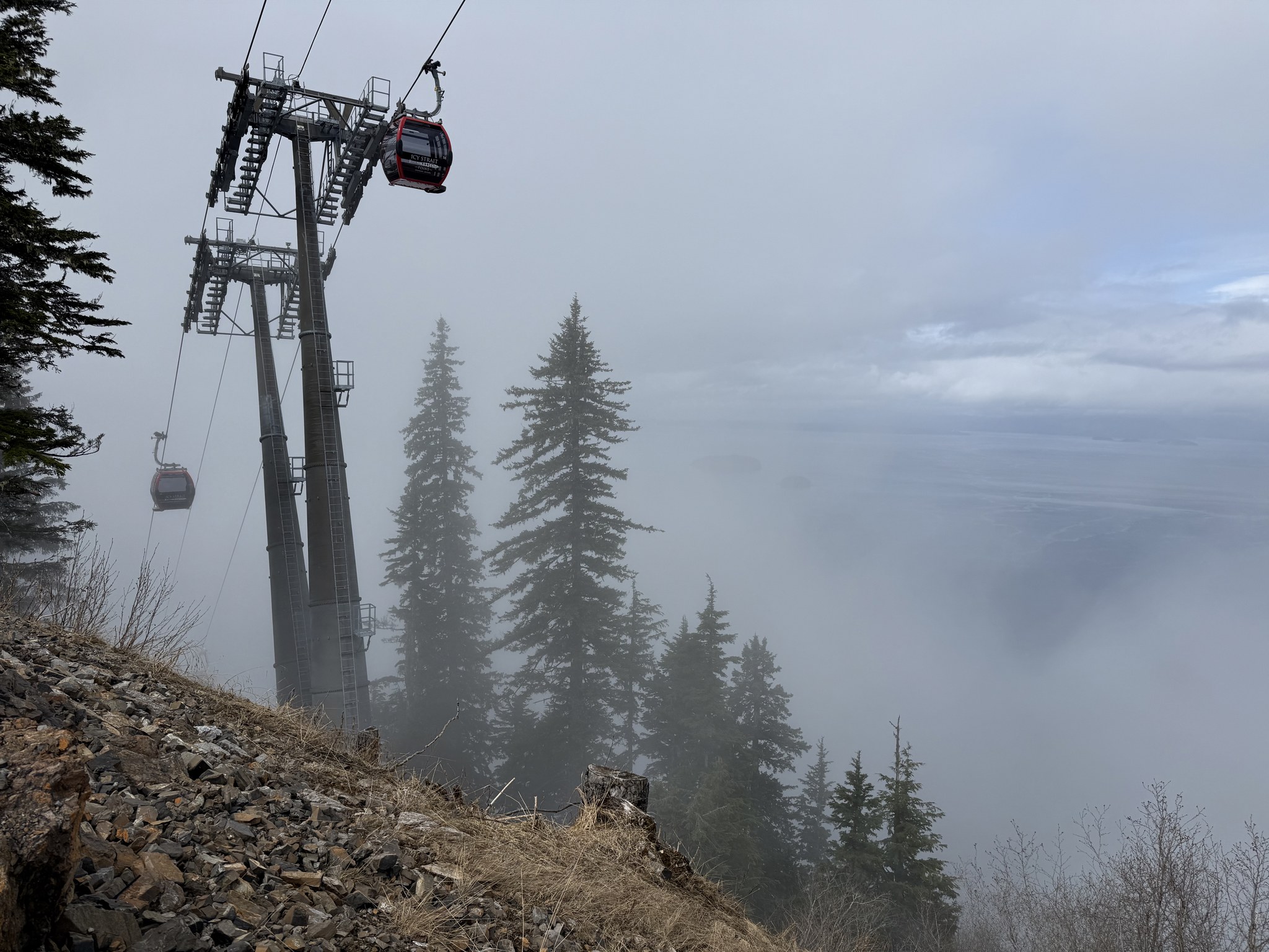 Red mountain gondola cabins climbing Hoonah Mountain into the fog, Icy Strait Point