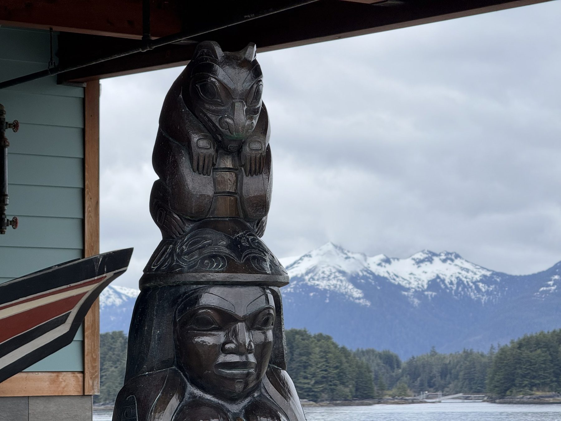 A carved totem figure with snowy mountains behind in Sitka